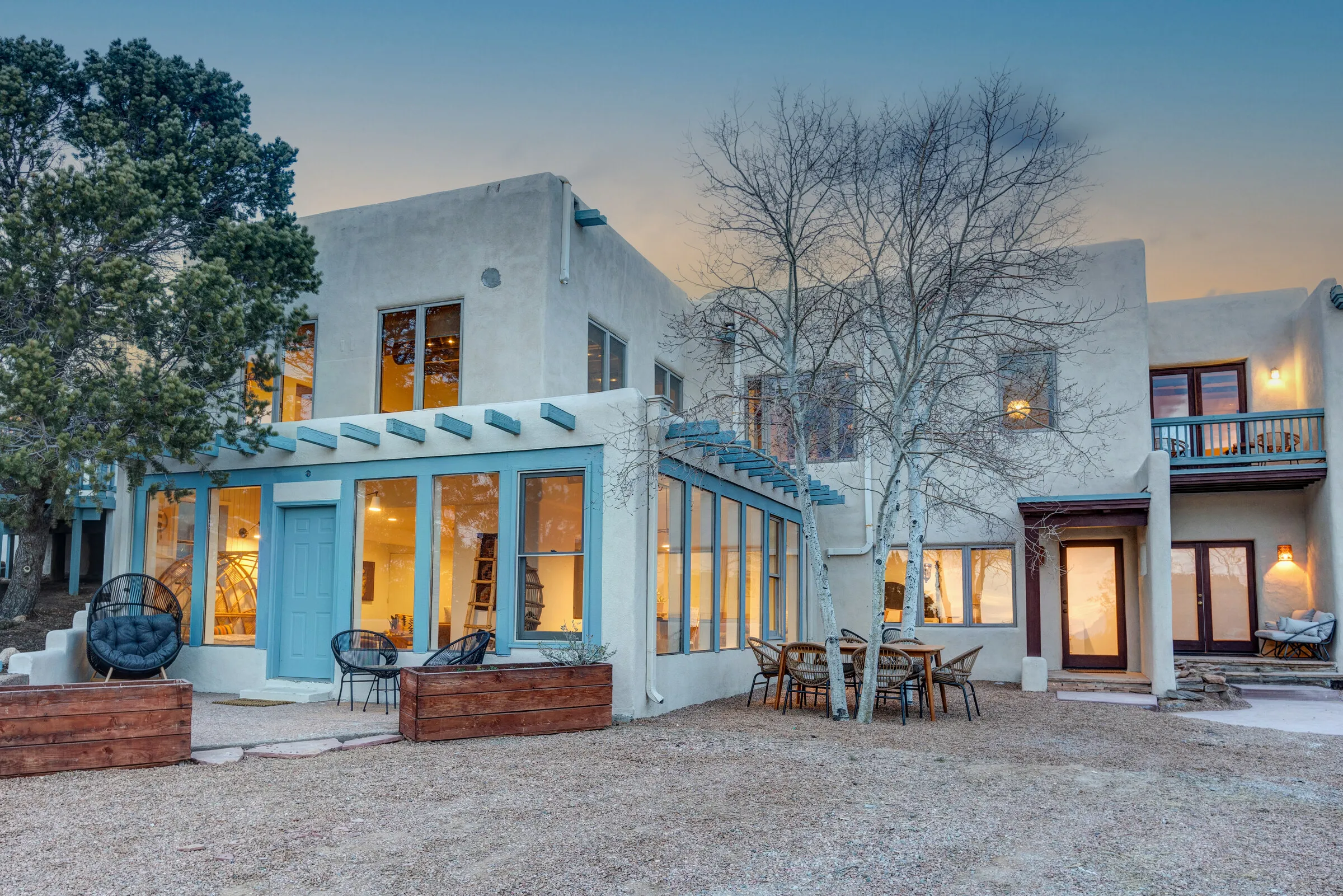 Casa de Camino at dusk — the two-story adobe with blue-trimmed windows glowing, the bare aspen out front
