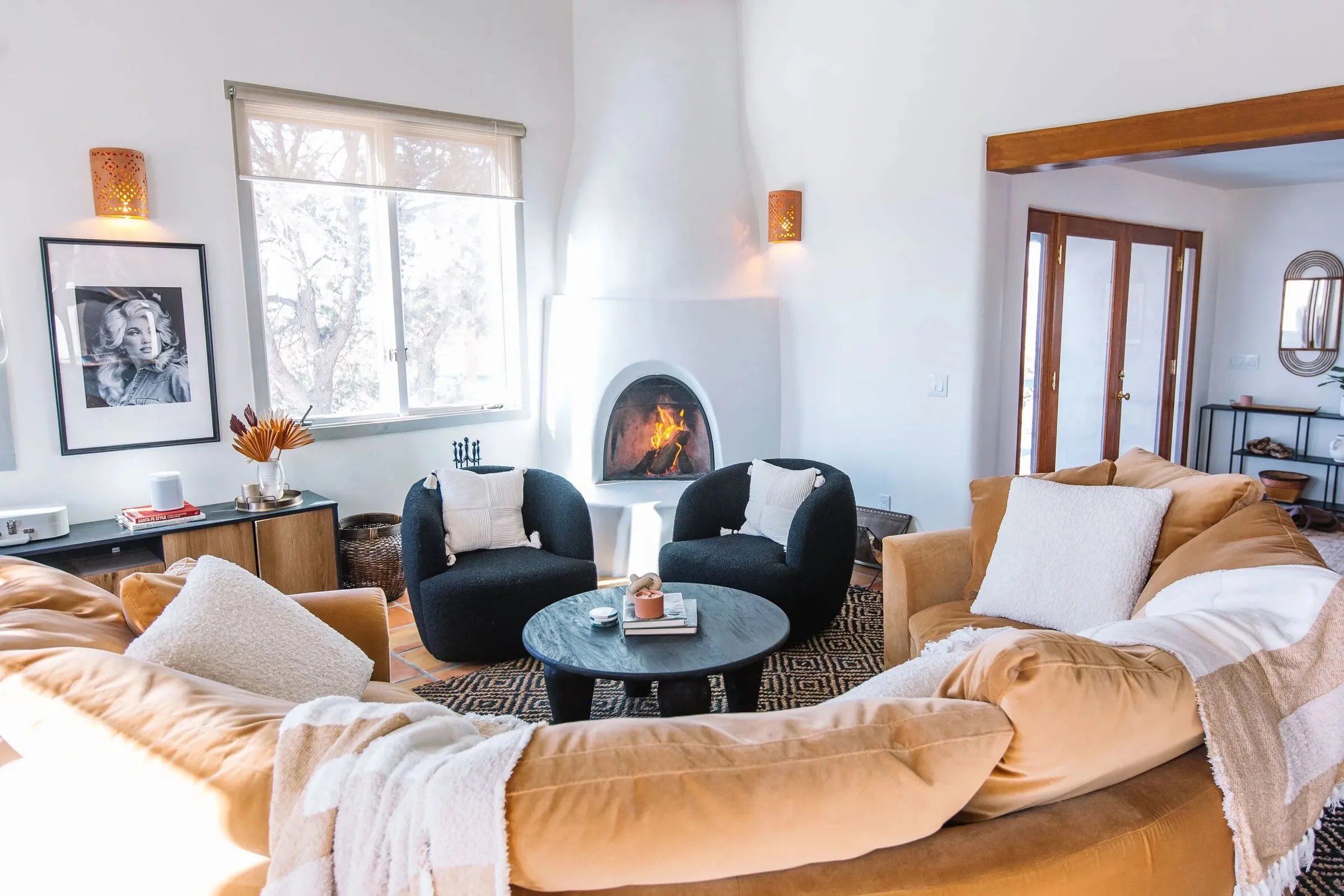 The living room at Casa de Camino — the round camel sofa under the log-viga ceiling, a kiva fire lit
