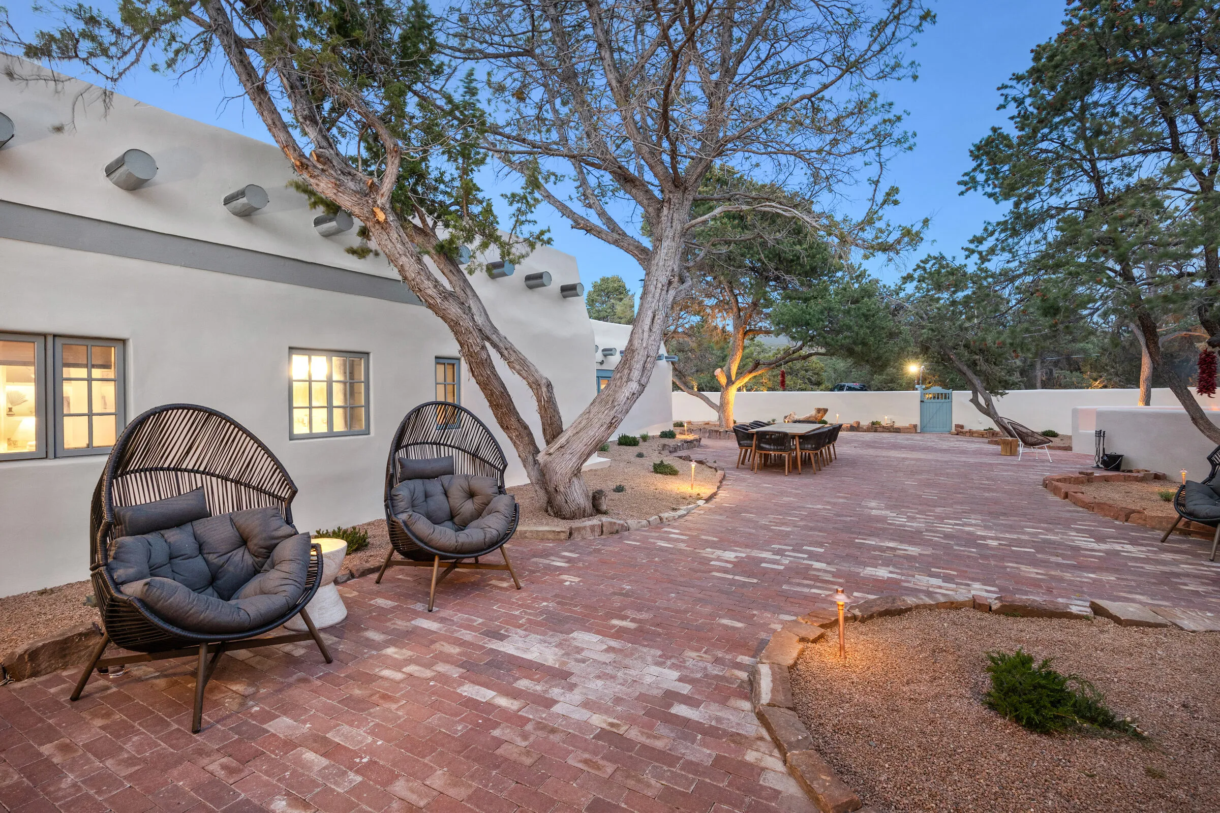 The Casa de Ice courtyard at dusk — fire pit lit, the adobe estate glowing behind the piñons