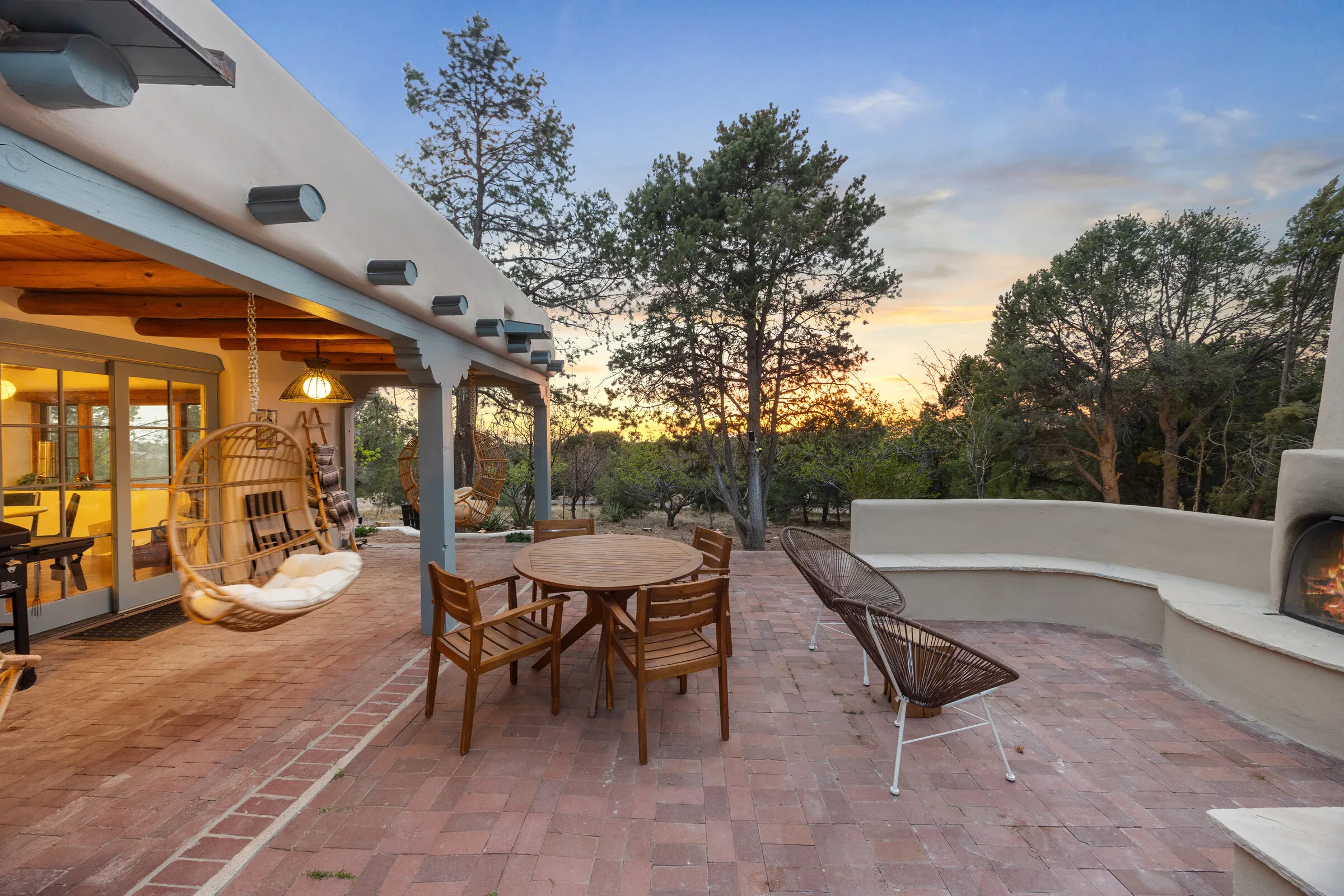 The portal at Casa de Ice at dusk — hanging chairs, a kiva fire going, sunset over the piñon