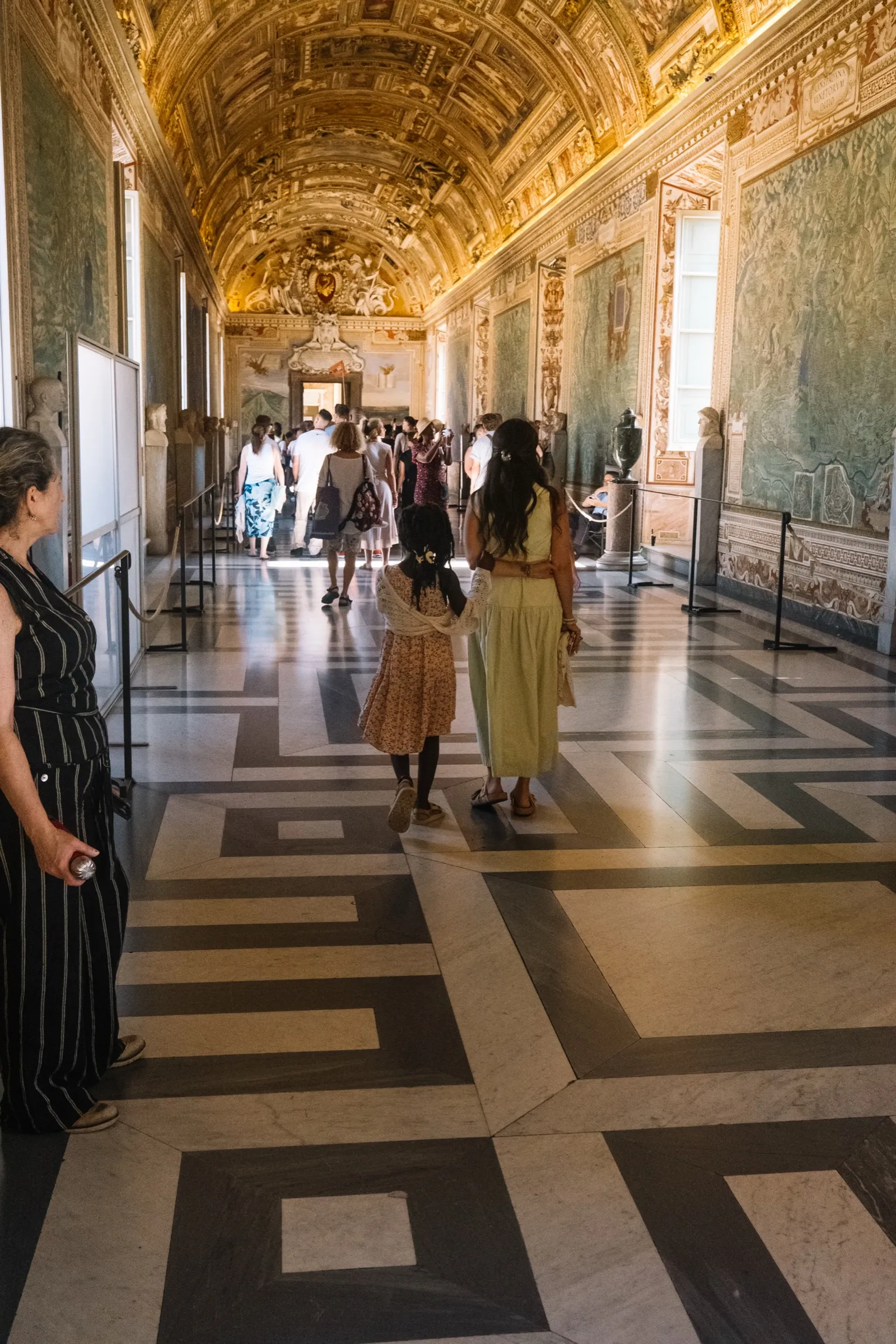 The Vatican's marble corridor and ornate ceiling, figures walking through