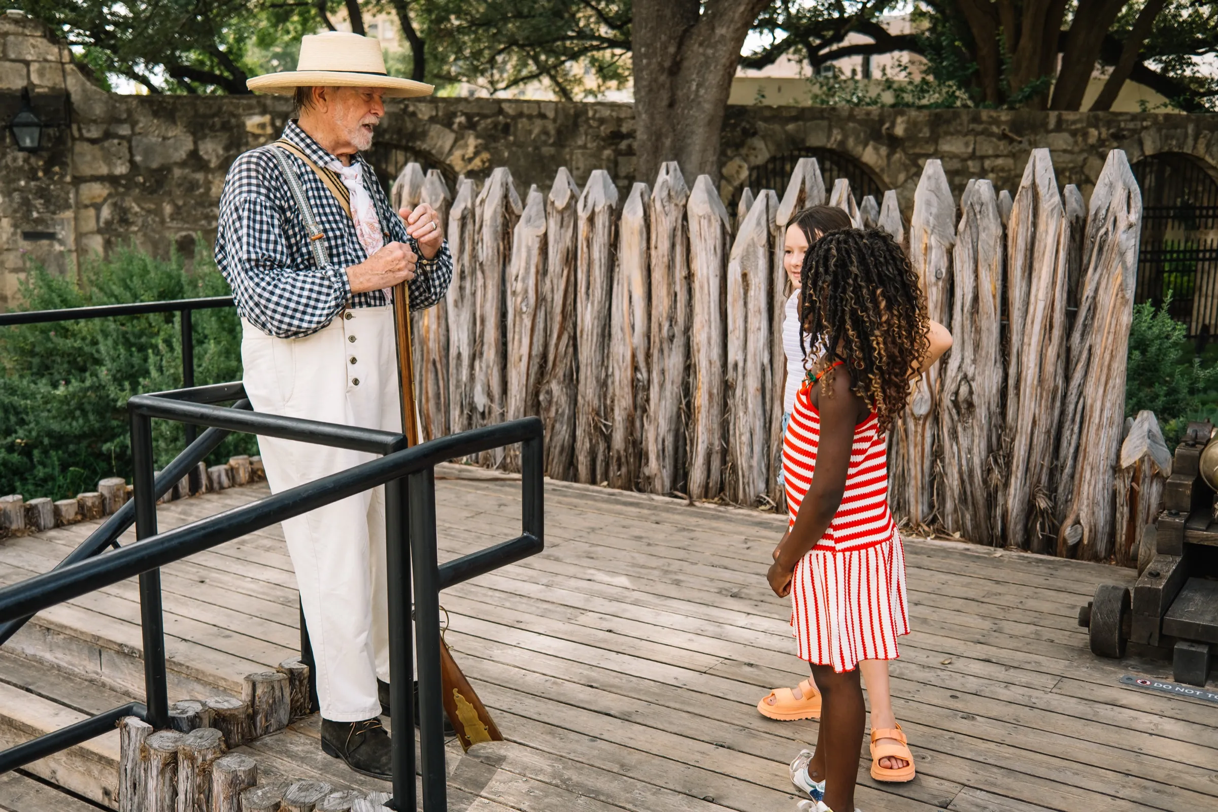 A living-history interpreter in period dress with his musket at the Alamo palisade, Justice and Rosie listening