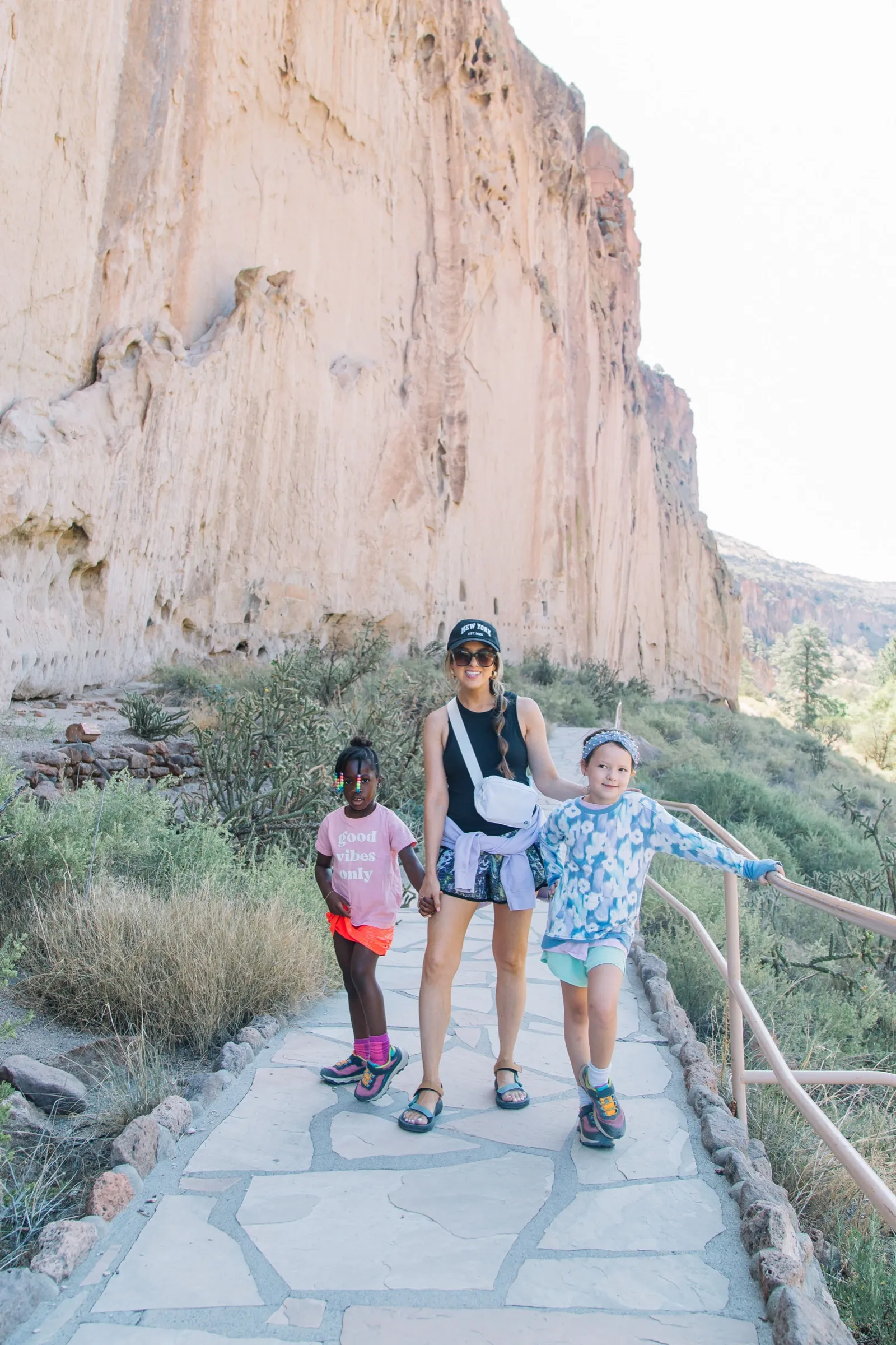 Melissa and the girls on the cliff path at Tsankawi, the mesa wall rising beside them